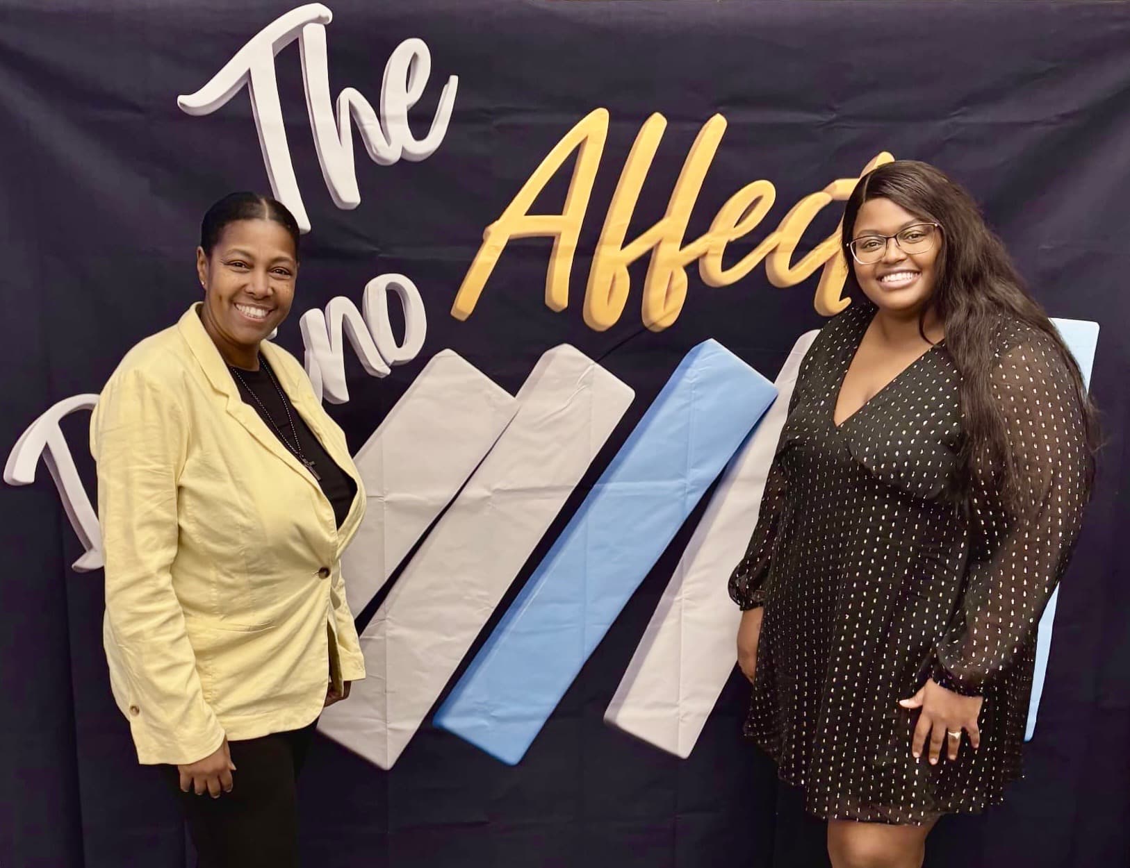 Dominique Whipple standing with another woman in front of The Domino Affect event backdrop